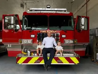 Florida firefighter seated with two children in front of a fire rescue truck
